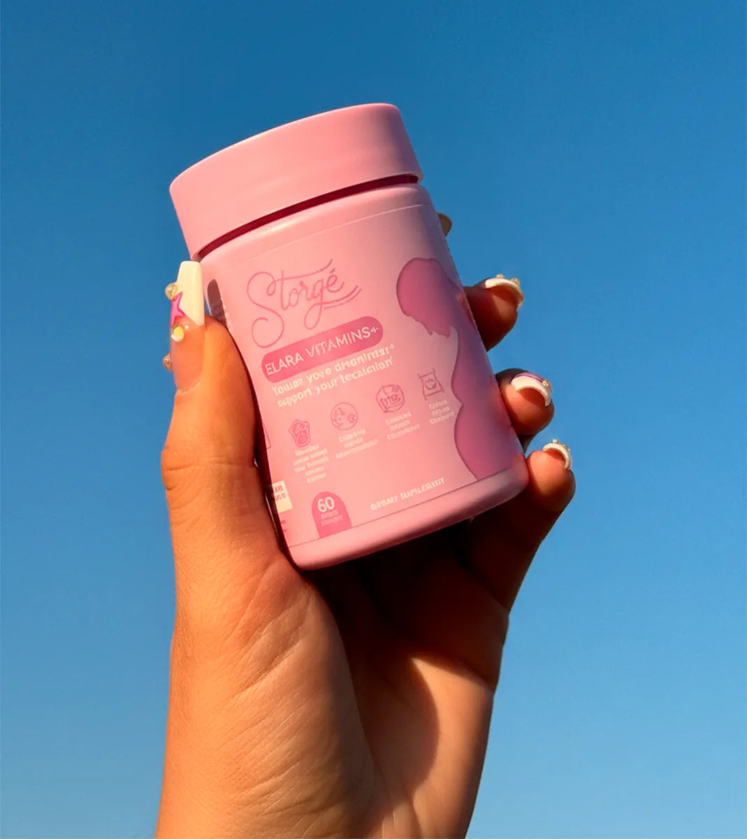 Hand holding Storgé Elara prenatal vitamins jar against blue sky, clean maternity wellness aesthetic
