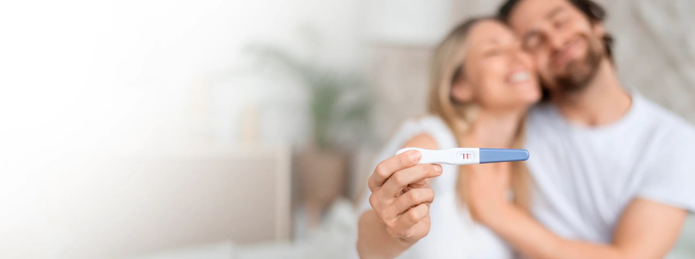 Happy couple holding positive pregnancy test at home, early pregnancy announcement moment