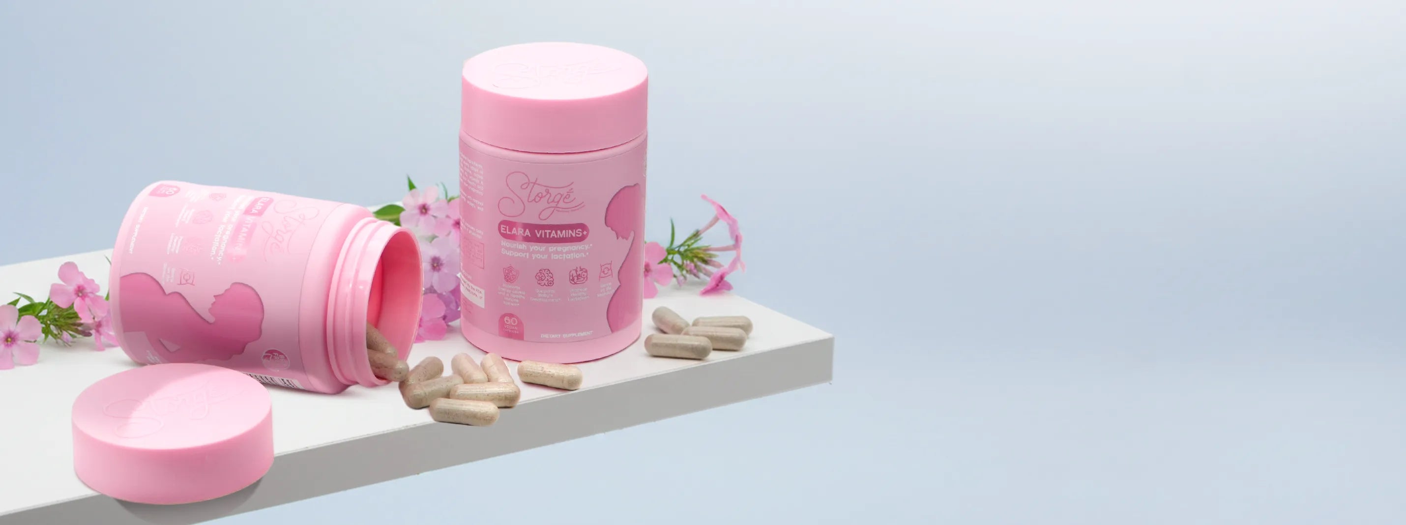 Pink prenatal vitamins supplement jars with capsules and flowers on white surface, premium maternity wellness product