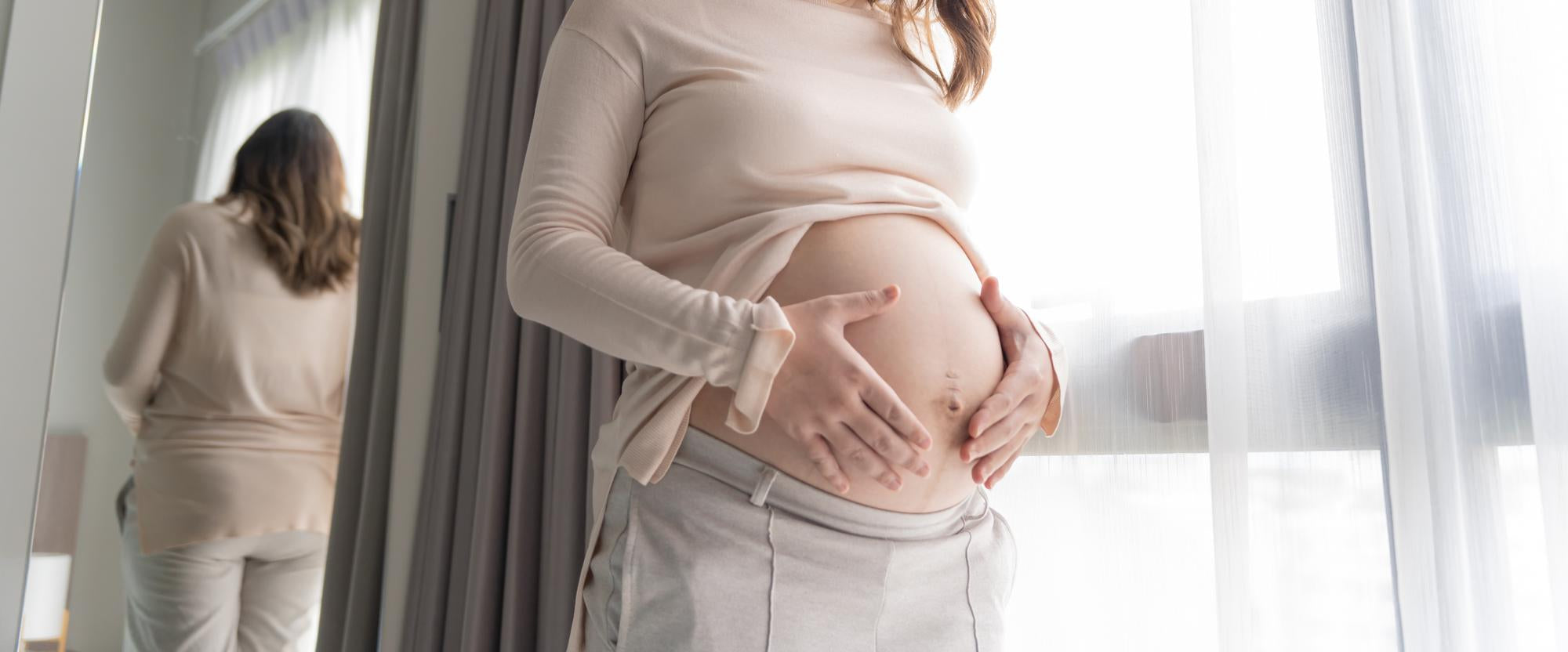 Pregnant woman gently holding her belly near window, peaceful maternity lifestyle and pregnancy wellness moment