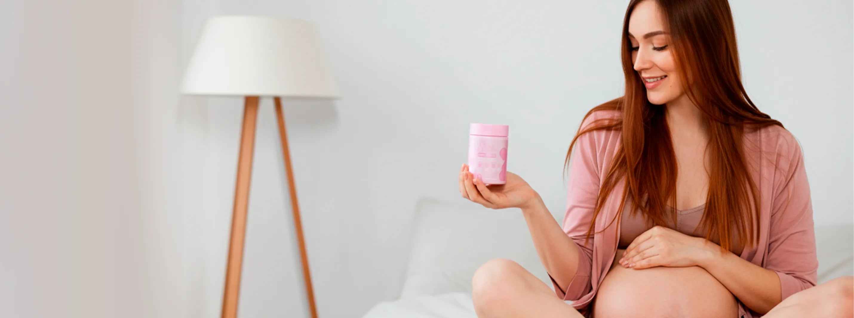 Pregnant woman holding pink prenatal vitamins jar in bedroom, daily maternity wellness routine