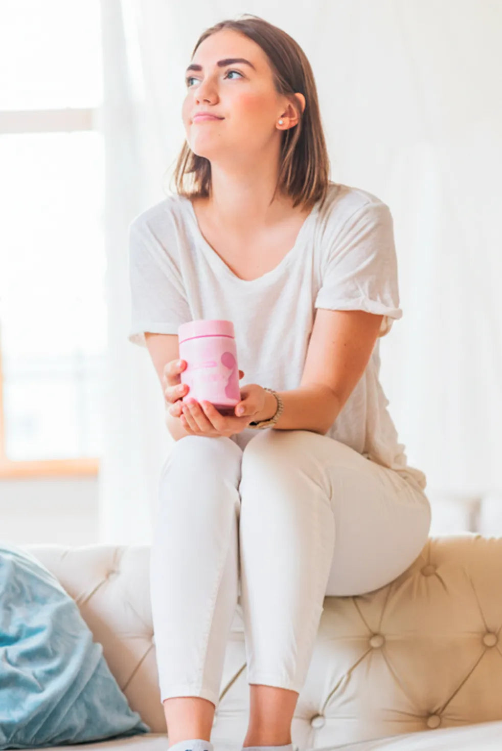 Woman sitting on sofa holding pink prenatal vitamins jar, daily pregnancy supplement lifestyle photo