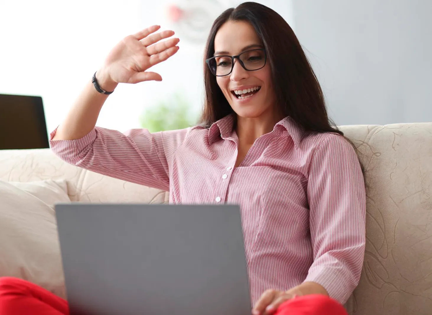 Woman waving during online video call on laptop, virtual women’s wellness support session