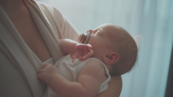 Newborn baby sleeping peacefully in mother’s arms, tender postpartum bonding moment